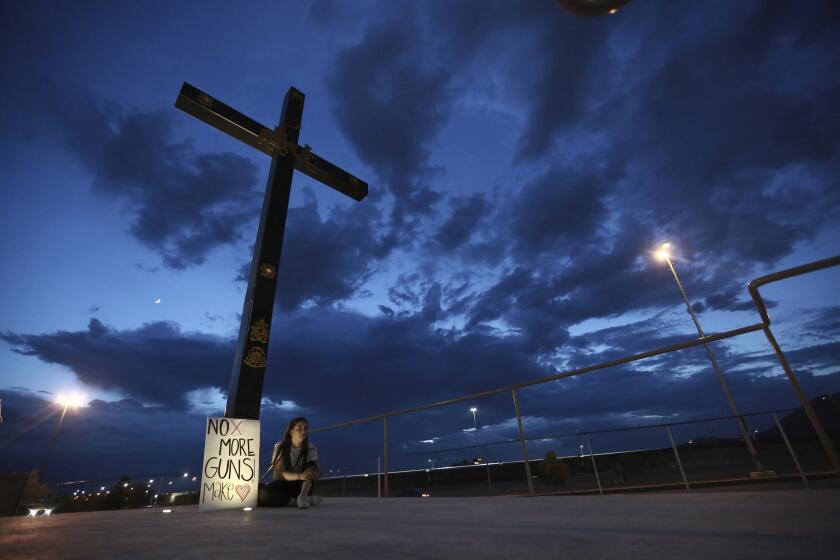 A woman sits next to a sign with a message that reads: (R)No More Guns! Make Love(R), in Juarez, Mexico, Saturday, Aug. 3, 2019, where people are gathering for a vigil for the 3 Mexican nationals who were killed in an El Paso shopping-complex shooting. Twenty people were killed and more than two dozen injured in a shooting Saturday in a busy shopping area in the Texas border town of El Paso, the state?s governor said. (AP Photo/Christian Chavez)