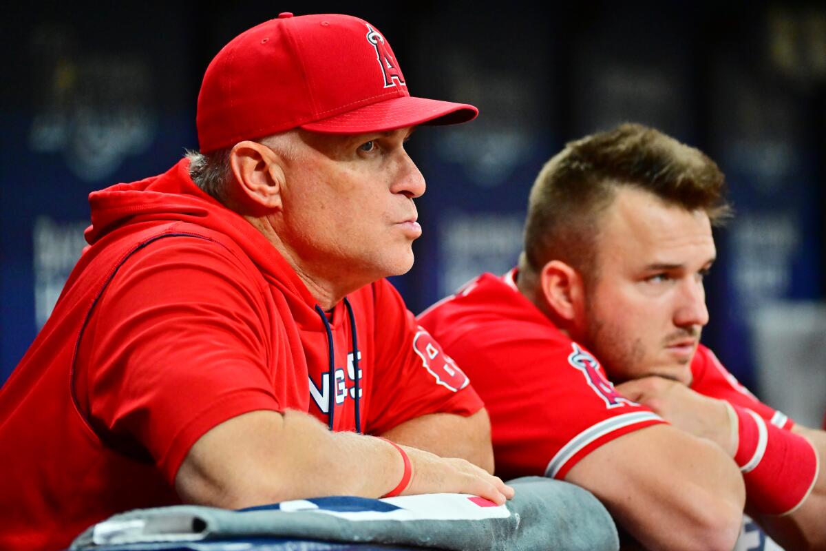 Angels manager Phil Nevin, left, stands next to Angels star Mike Trout in the dugout during a game.