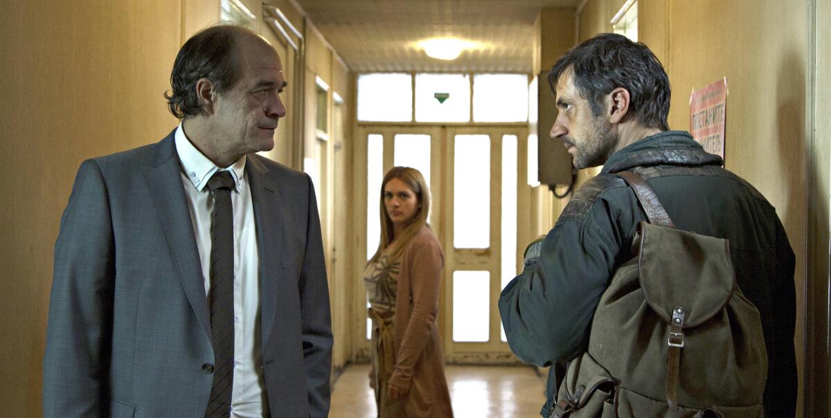 A woman watches as a man in a suit faces off with a man with a rucksack in a hallway in the 2020 drama “Father.” 