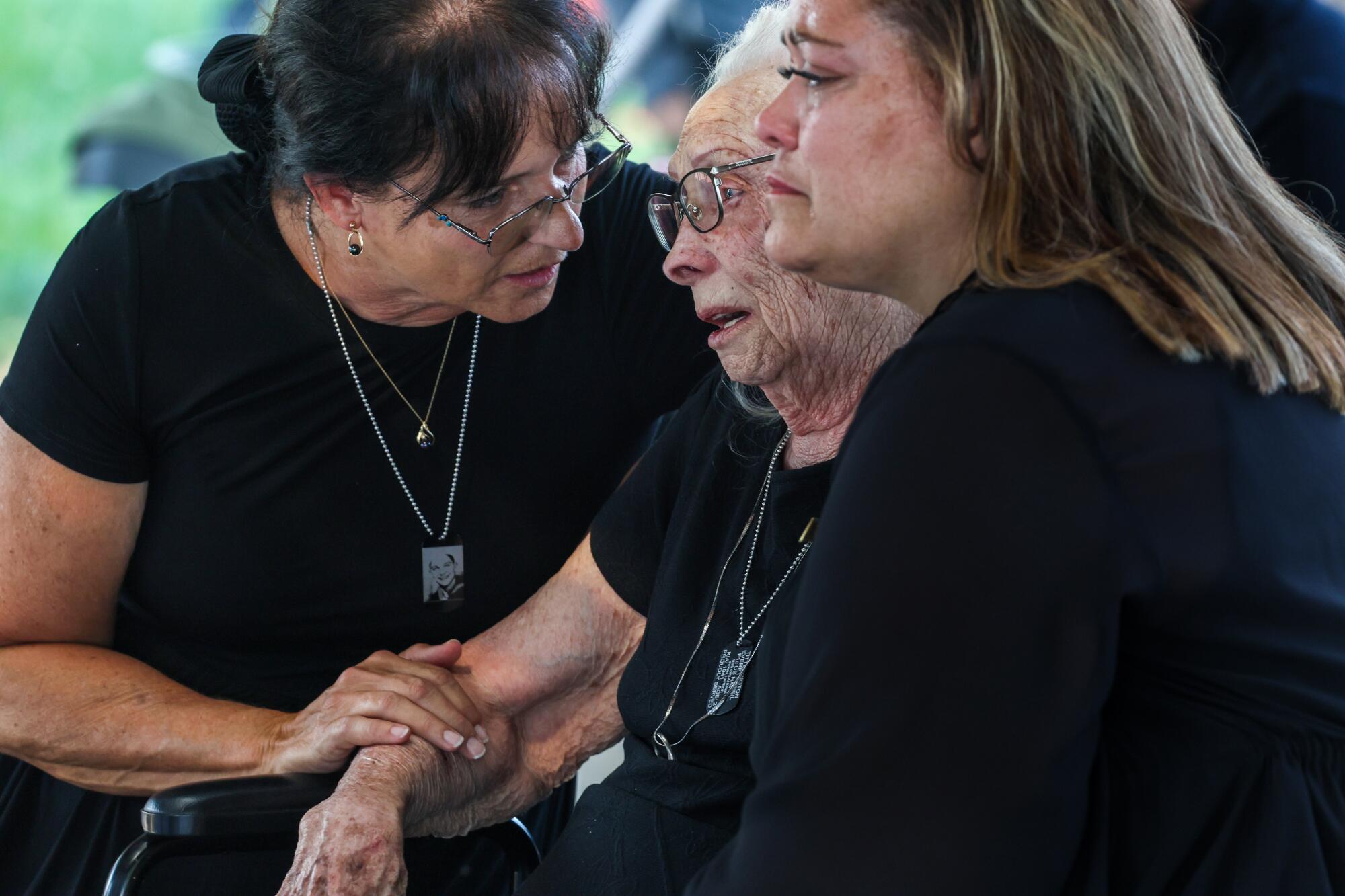 An elderly woman in glasses, who is crying, is flanked by two other women, also wearing black 