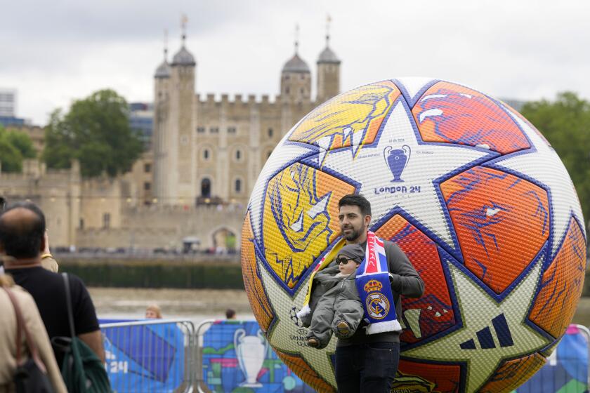 Football fans pose by a giant Champions League football at the Champions Festival in Potters Fields Park near Tower Bridge in London, Thursday, May 30, 2024. The Champions League soccer final between Dortmund and Real Madrid will take place at Wembley Stadium on Saturday June 1. (AP Photo/Kirsty Wigglesworth)