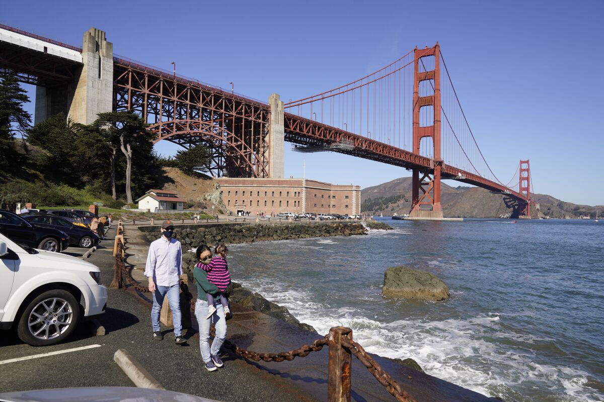 FILE - People walk along a seawall with Fort Point and the Golden Gate Bridge in the background in San Francisco, on Oct. 11, 2020. The lead contractor in charge of building a suicide prevention net on San Francisco’s Golden Gate Bridge that is already years behind schedule says it will cost about $400 million, more than double its original price, because of deterioration that was concealed and other problems. (AP Photo/Eric Risberg, File)
