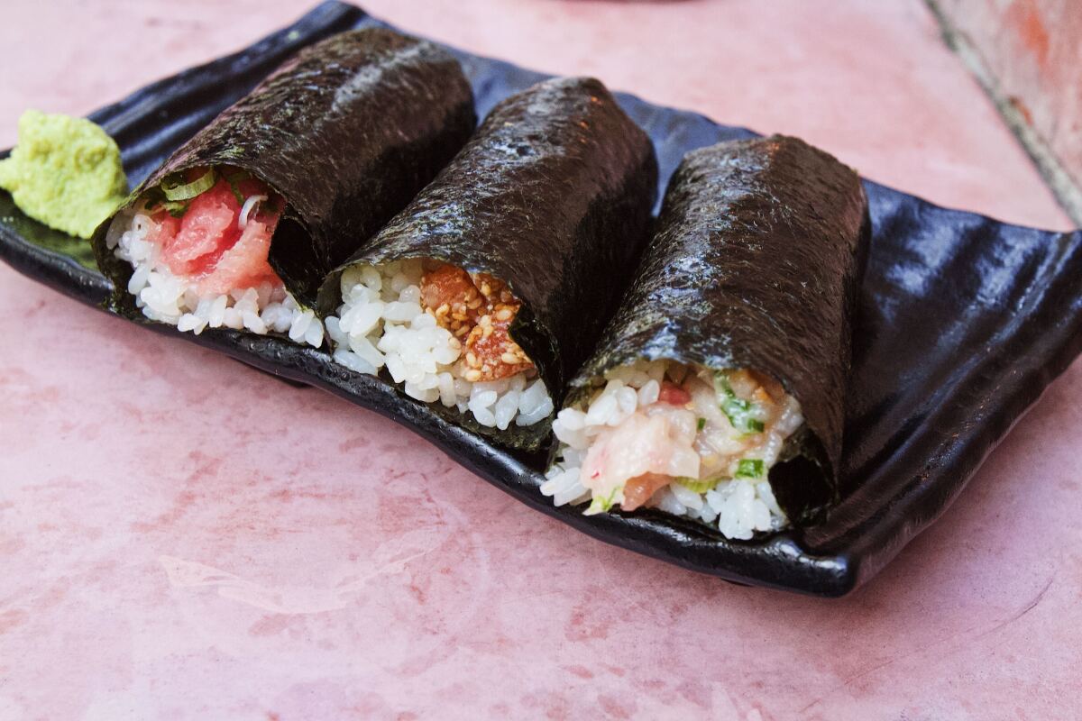 A trio of seaweed-wrapped hand rolls on a wavy black ceramic plate with a dollop of wasabi.