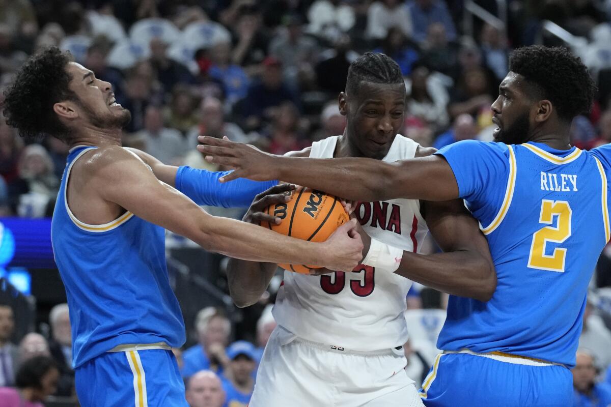 UCLA's Johnny Juzang, left, and Cody Riley, right, try to contain Arizona's Christian Koloko during the first half.