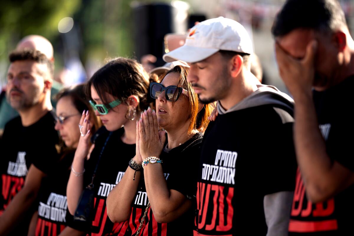 People stand in a line, wearing black T-shirts with white and red Hebrew lettering, praying.