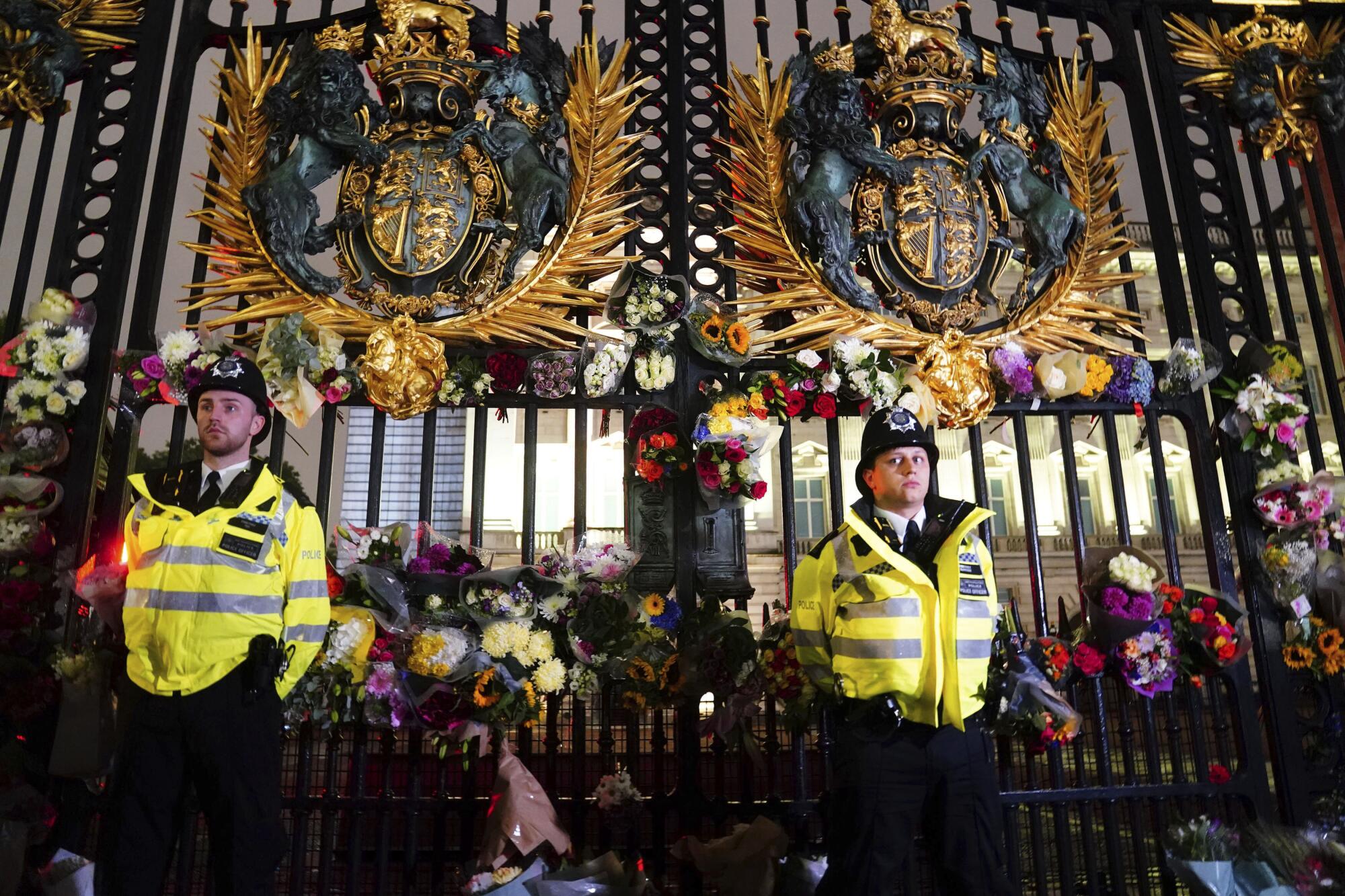 Police officers stand among floral tributes left outside Buckingham Palace.