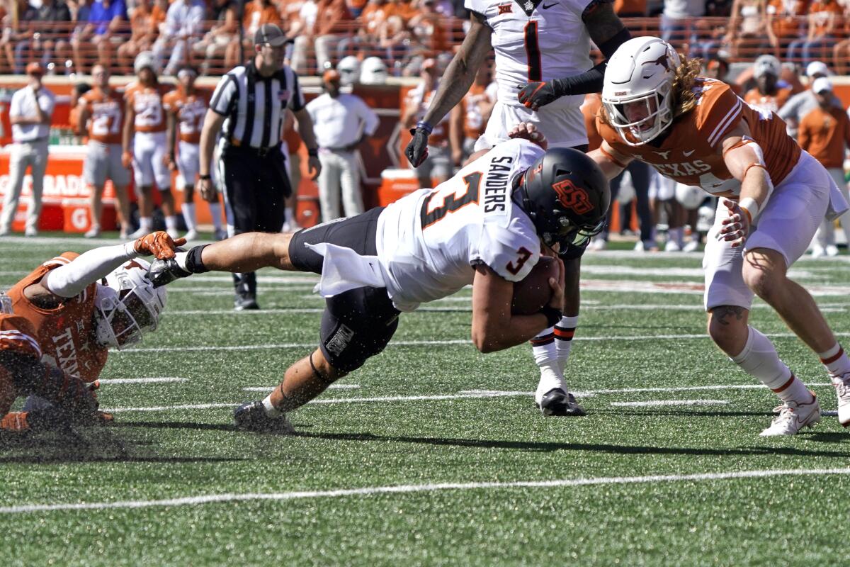 Oklahoma State quarterback Spencer Sanders is tackled by Texas defensive backs Josh Thompson and Brenden Schooler.