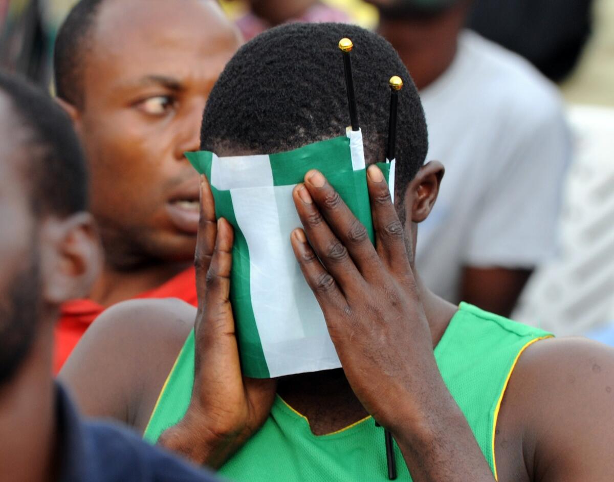 A Nigeria fan covers his face with the country's green and white flag as he watches the World Cup round of 16 game against France in Lagos, Brazil. France won the game, 2-0.