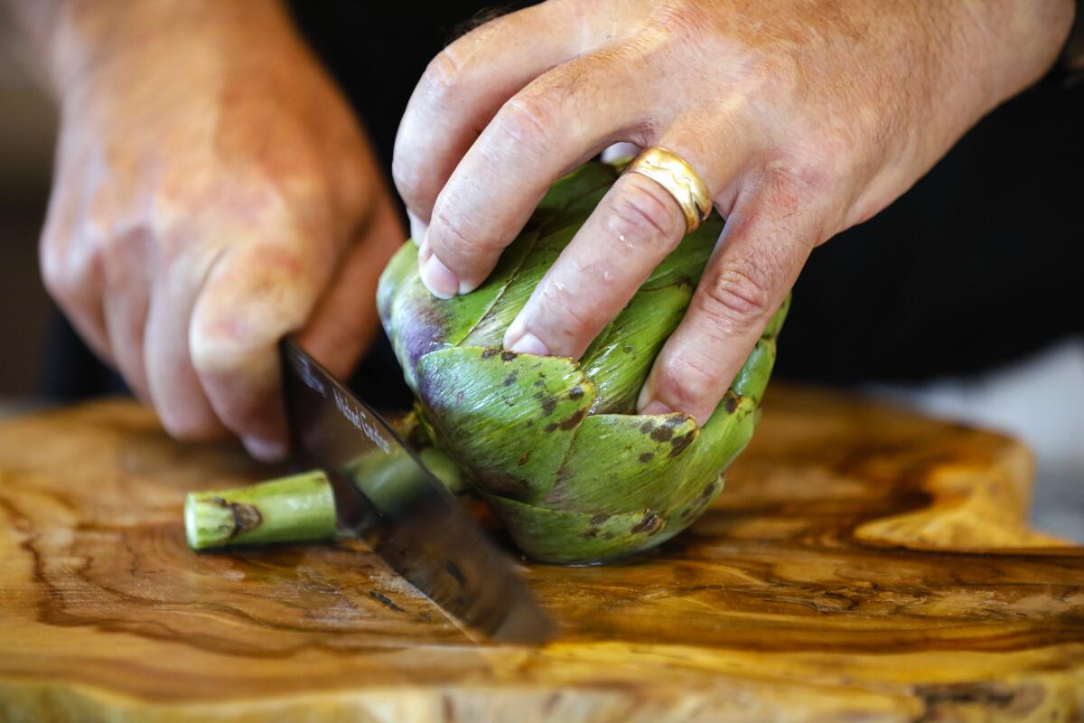 Slicing off all but the top inch of the stem of a whole globe artichoke.