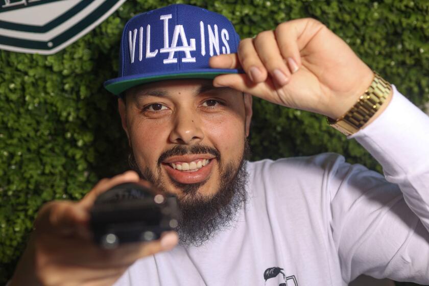 South Gate, CA - April 02: Villains Barber Shop Owner Anthony Madrid poses for a portrait at Villains Barbershop on Tuesday, April 2, 2024 in South Gate, CA. The villains cap with the LA Dodgers logo in the middle went semi-viral during one of the spring training games when a camera caught a fan wearing one. (Michael Blackshire / Los Angeles Times)