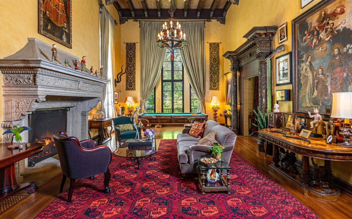 The living room with a fireplace, colorful rug, paintings, furniture and window overlooking greenery.