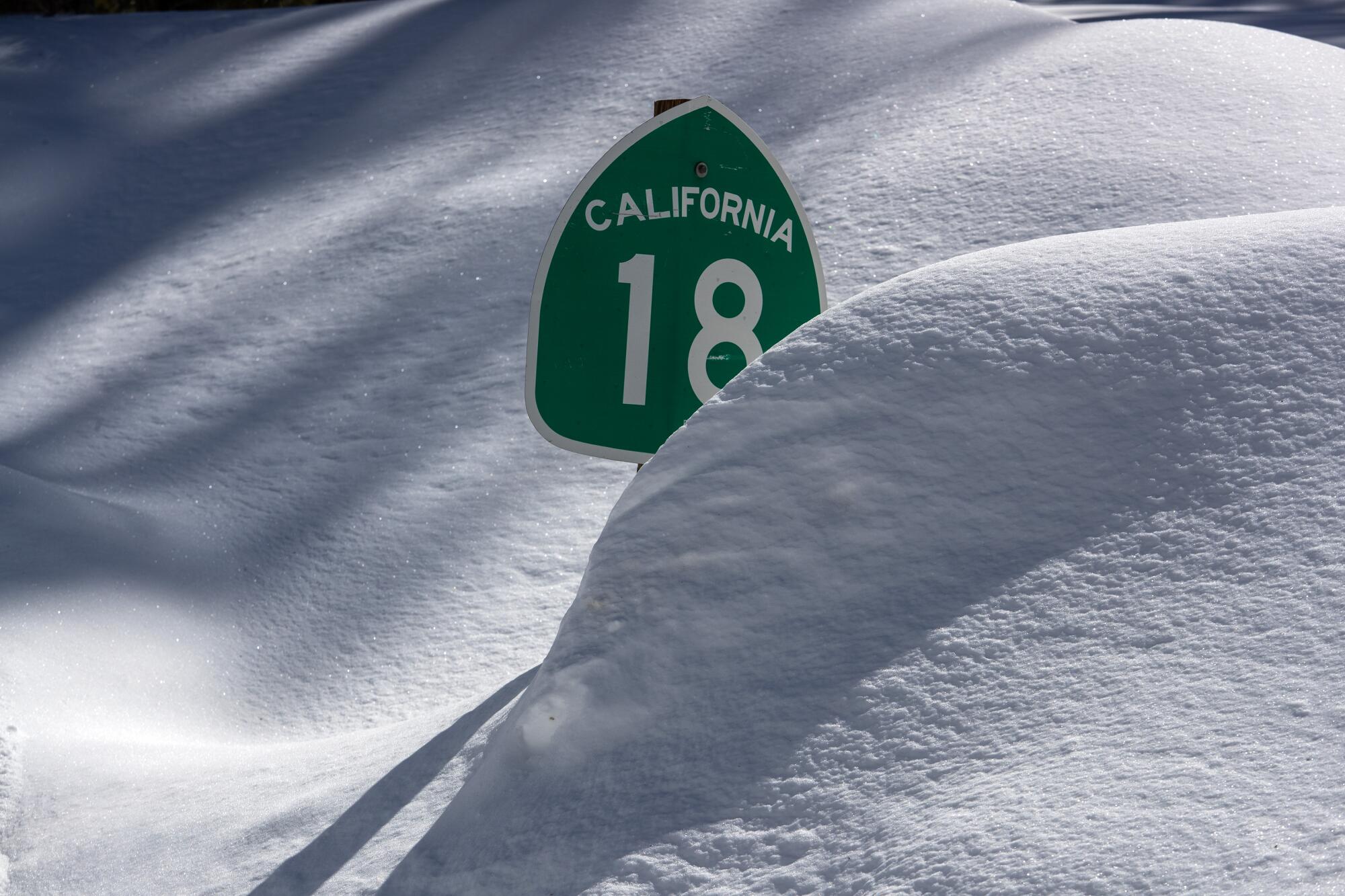 A signs that says "California 18" is poking out of a large, soft pile of snow.
