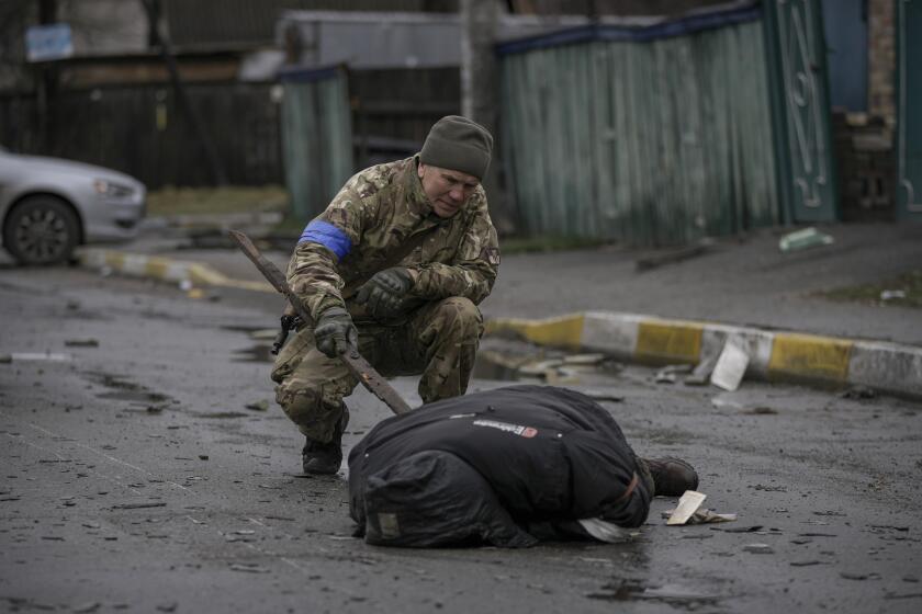 A Ukrainian serviceman uses a piece of wood to check if the body of a man dressed in civilian clothing is booby-trapped with explosive devices, in the formerly Russian-occupied Kyiv suburb of Bucha, Ukraine, Saturday, April 2, 2022. As Russian forces pull back from Ukraine's capital region, retreating troops are creating a "catastrophic" situation for civilians by leaving mines around homes, abandoned equipment and "even the bodies of those killed," President Volodymyr Zelenskyy warned Saturday.(AP Photo/Vadim Ghirda)