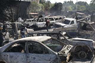 Varias personas buscan piezas rescatables de coches quemados en un taller mecánico incendiado durante la violencia desatada por pandillas armadas en Puerto Príncipe, Haití, el lunes 25 de marzo de 2024. (AP Foto/Odelyn Joseph)