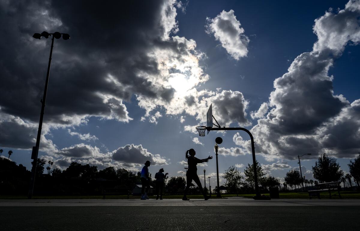 People are playing basketball as the sun peeks through clouds.