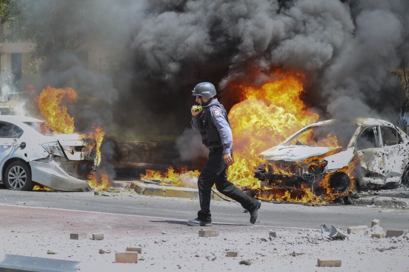 An Israeli firefighter walks next to cars hit by a missile fired from Gaza Strip, in the southern Israeli town of Ashkelon, Tuesday, May 11, 2021. (AP Photo/Ariel Schalit)