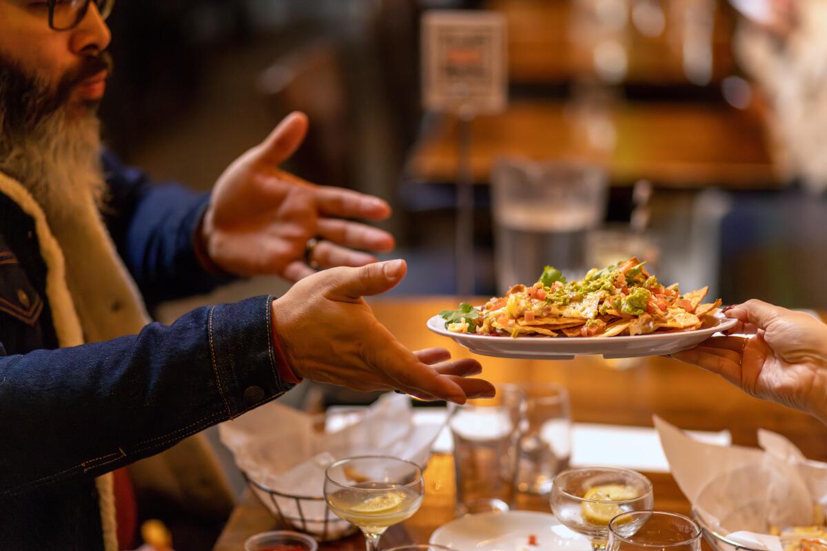 One person hands another a plate loaded with nachos.
