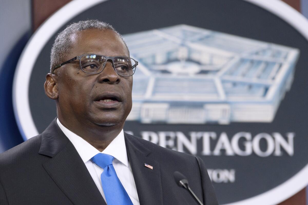 A closeup of Lloyd Austin, in suit and tie, speaking into a microphone with the Pentagon logo behind him.