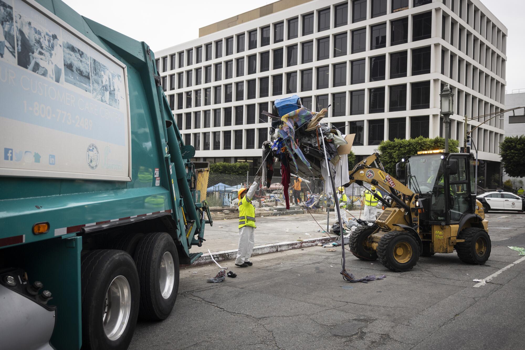 Un cargador de construcción que transporta los restos de un campamento a un camión de basura de la ciudad