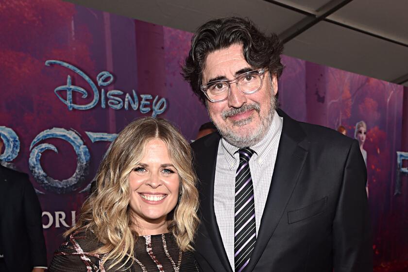 A shorter woman and a taller man pose on a red carpet