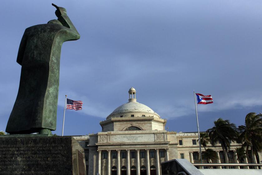 ARCHIVO - Una estatua de bronce de San Juan Bautista frente al Capitolio, flanqueada por banderas de Estados Unidos y Puerto Rico, en San Juan, Puerto Rico. (AP Foto/Ricardo Arduengo, Archivo)