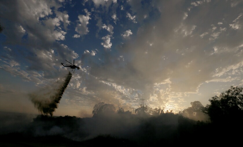 A firefighting helicopter makes a water drop on a wildfire burning in the hills around Idaho Street in La Habra.