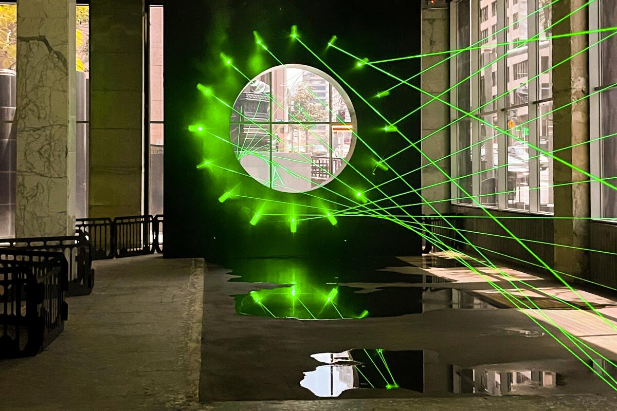 An installation piece by Rita McBride shows green laser lights emerging around a circle cut into a wall