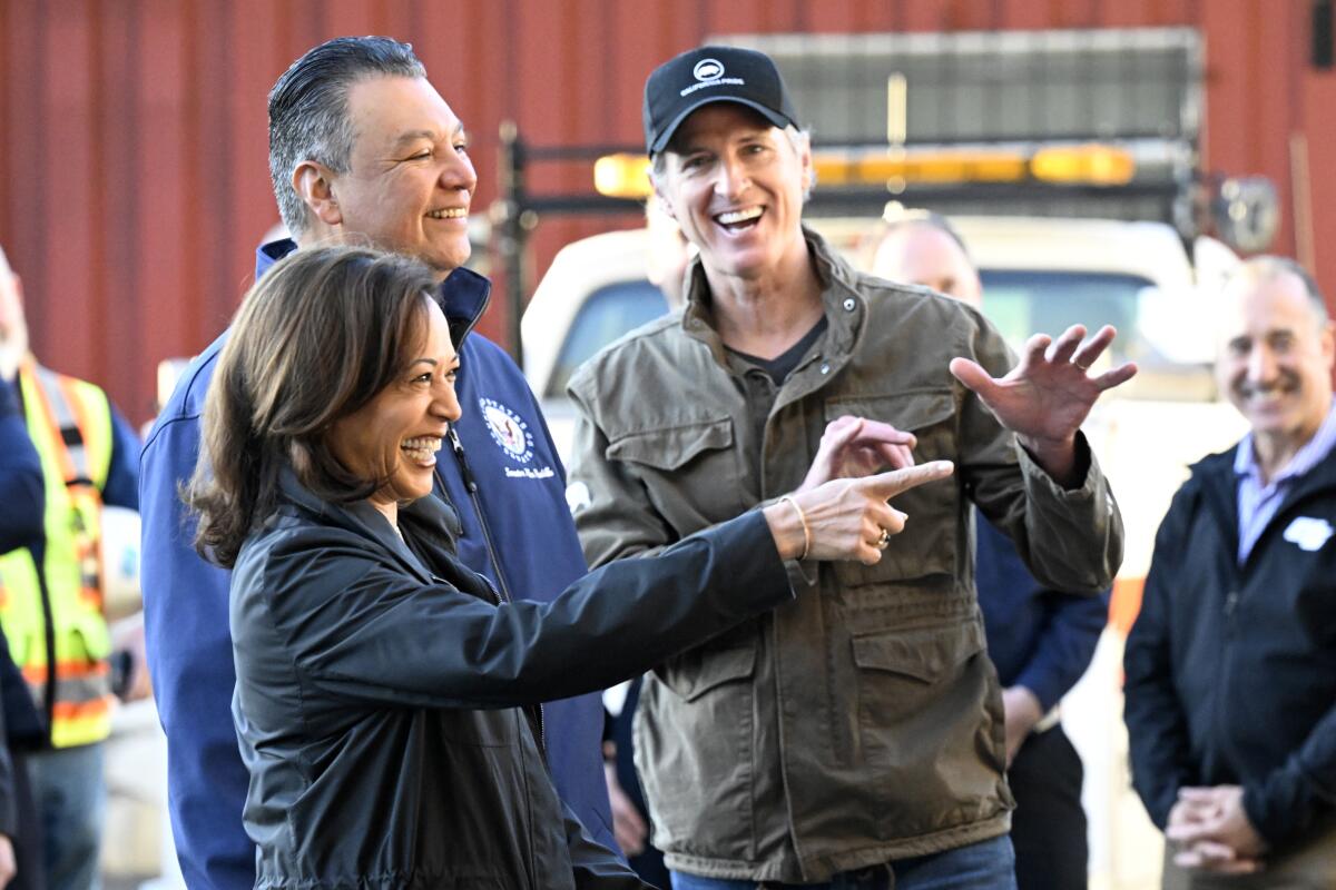 Kamala Harris, Sen. Alex Padilla and Gavin Newsom wearing casual jackets and laughing while visiting an outdoor project site