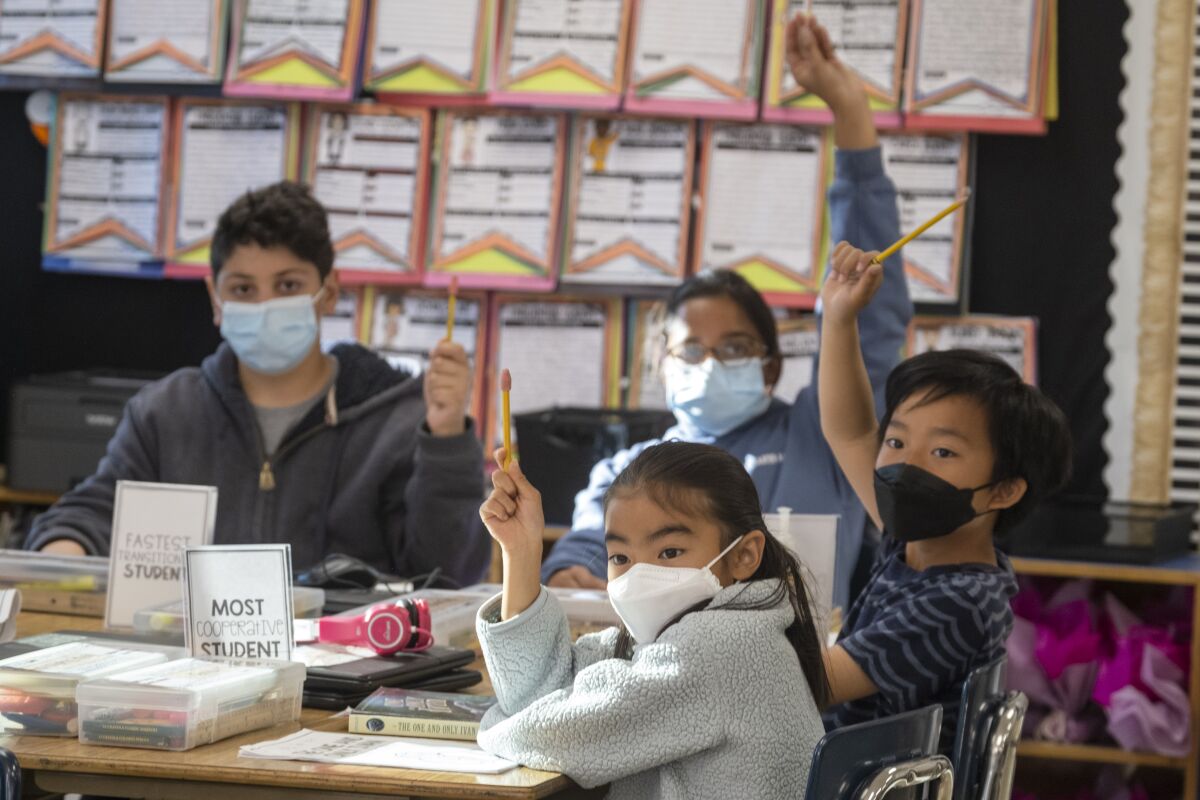 Masked students sitting at a table raise their hands