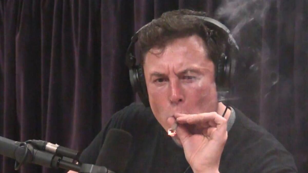 Tesla CEO Elon Musk smokes while next to a microphone.