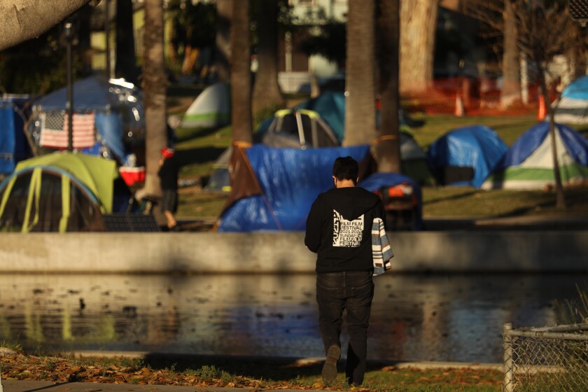 A visitor to Echo Park Lake takes a walk against a backdrop of tents where homeless people have taken up residence 