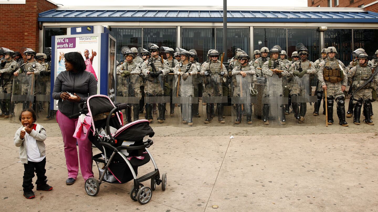 A woman and her child stand at the corner in Baltimore where a heavy police and National Guard presence was in place.