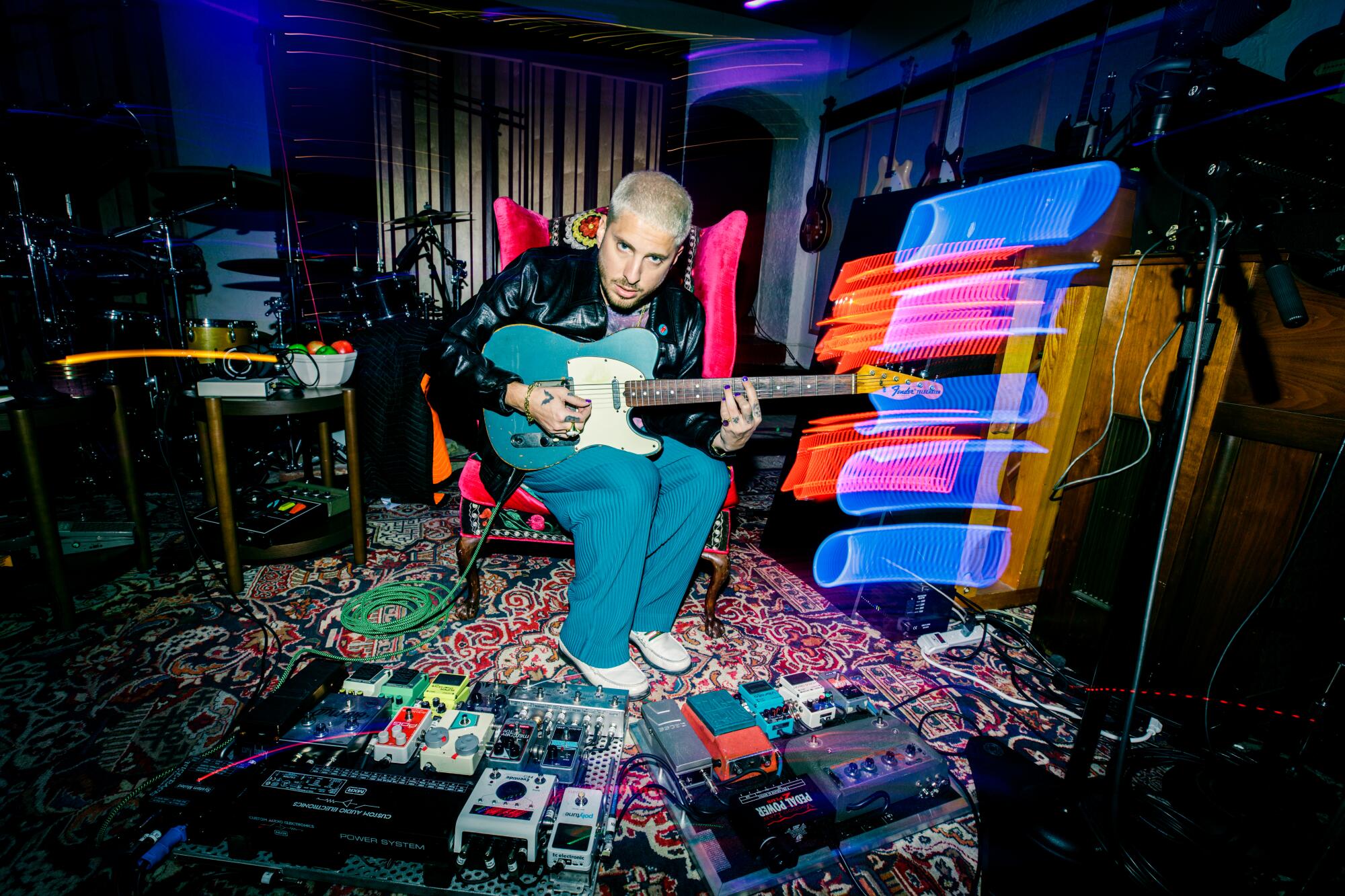 A producer/musician in his studio, playing electric guitar and surrounded by effects pedals.