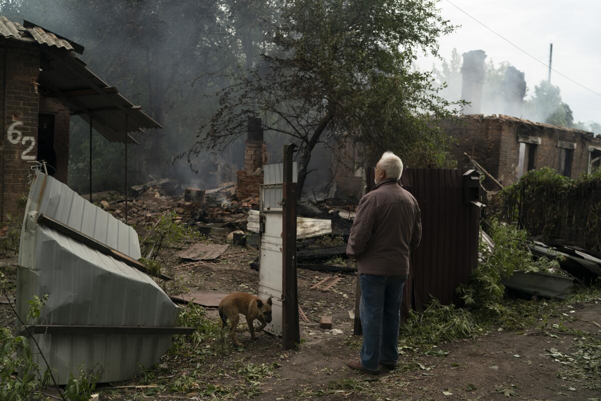 A man and a dog stand outside the rubble of a home.