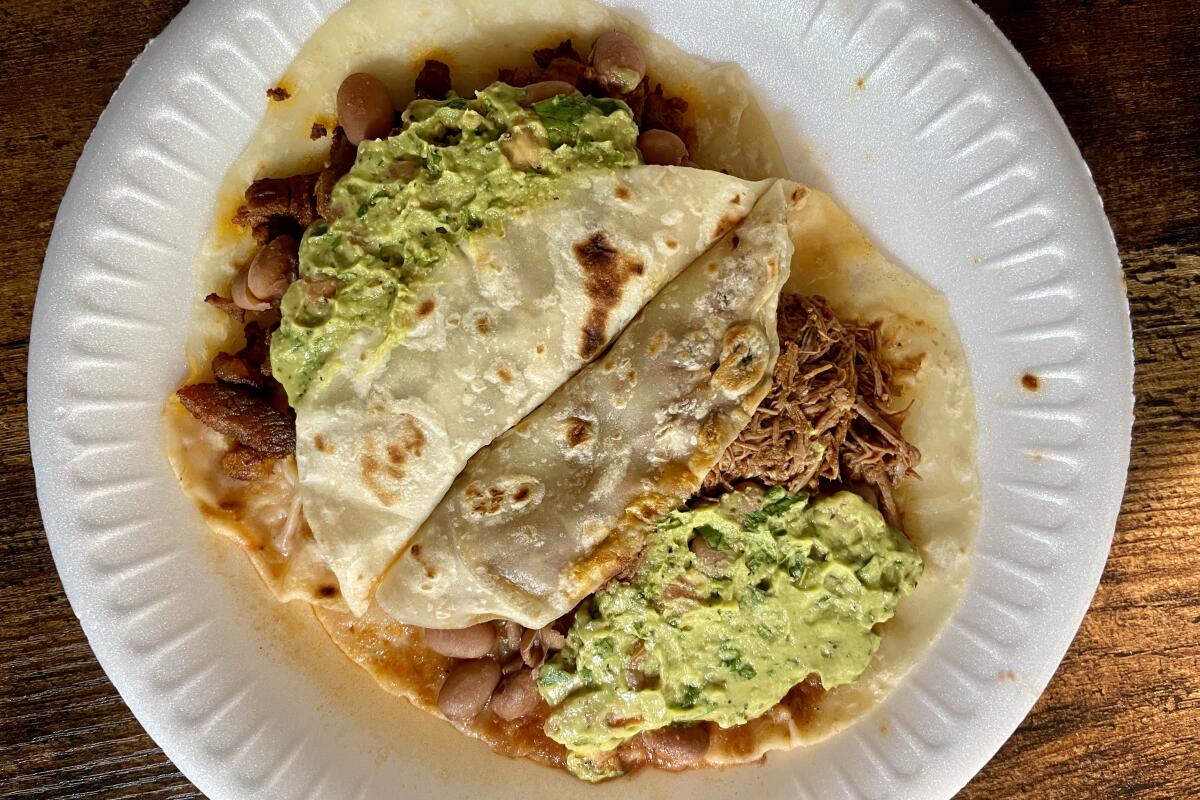 Two tacos on a paper plate with globs of guacamole on either side