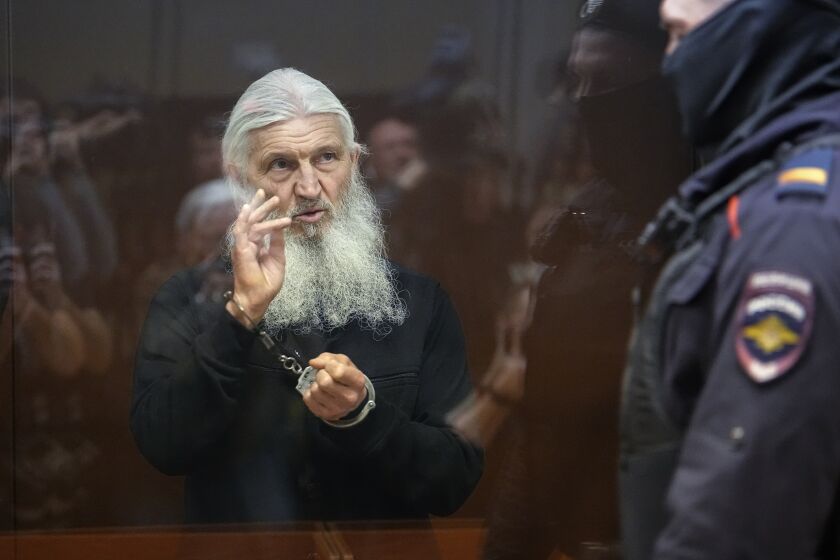 Nikolai Romanov, a former monk known as Father Sergiy until he was excommunicated by the Russian Orthodox Church, baptizes those present in the hall from behind a glass cage during his trial in Moscow, Russia, Friday, Jan. 27, 2023. The monk, who denied that the coronavirus existed and challenged the Kremlin, was handed a new prison sentence Friday on charges of inciting hatred. (AP Photo/Alexander Zemlianichenko)