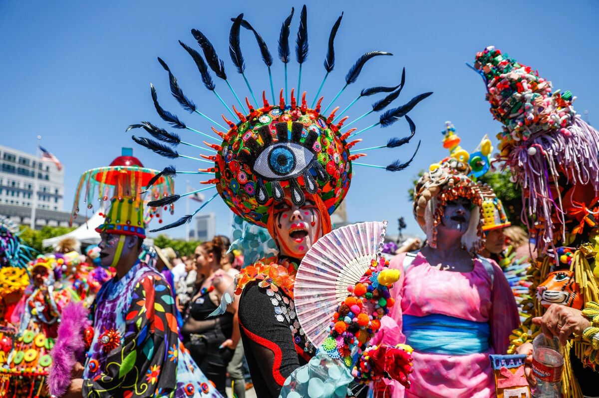 A woman wearing a hat in the shape of an eye fans herself amid a crowd of people in colorful costumes