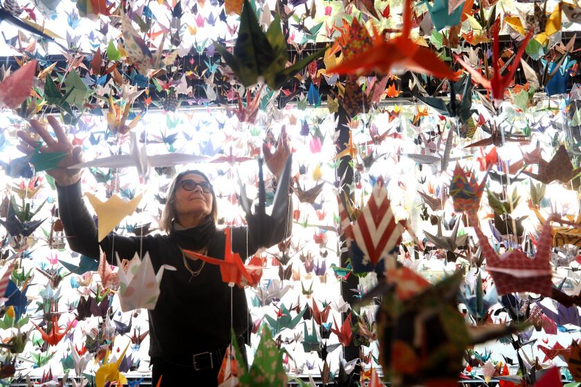 LOS ANGELES, CA - FEBRUARY 9, 2021 - - Karla Funderburk, owner of Matter Studio and Gallery, is surrounded by hundred of cranes that make up, "A Memorial for COVID-19 Victims," at her studio in Los Angeles on February 9, 2021. Funderburk has hung tens of thousands of paper cranes to commemorate those who have died from COVID-19. At first she folded them herself but once she realized it would take decades to make enough, she put out a call for people to send them to her. She's collected upward of 60,000 cranes from 45 different states and nine countries. She is in talks with multiple states to do installations of cranes, names and recordings, which people can listen to by scanning a QR code. (Genaro Molina / Los Angeles Times)