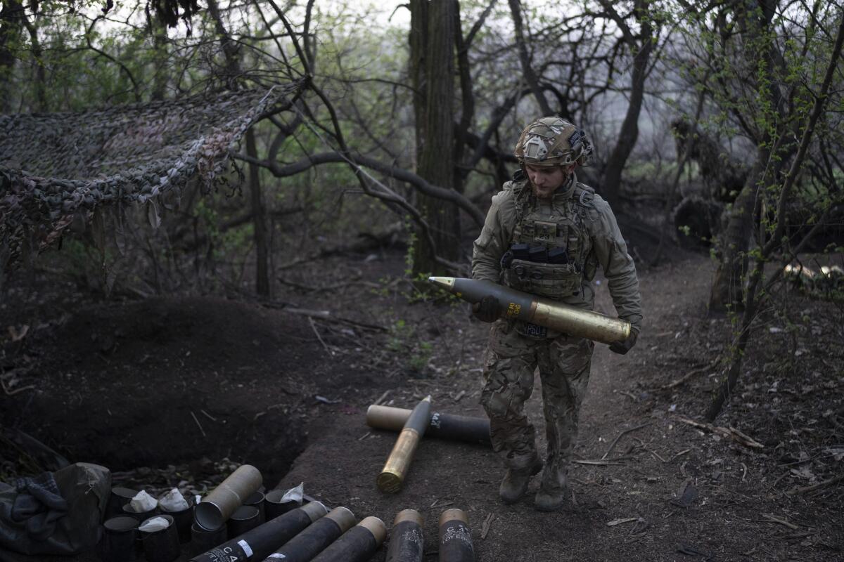 A Ukrainian serviceman carries a shell for the OTO Melara Mod 56 howitzer on the frontline in a wooded area.