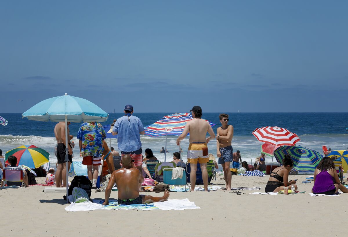 People standing and sitting at the beach under umbrellas for Fourth of July in San Diego.
