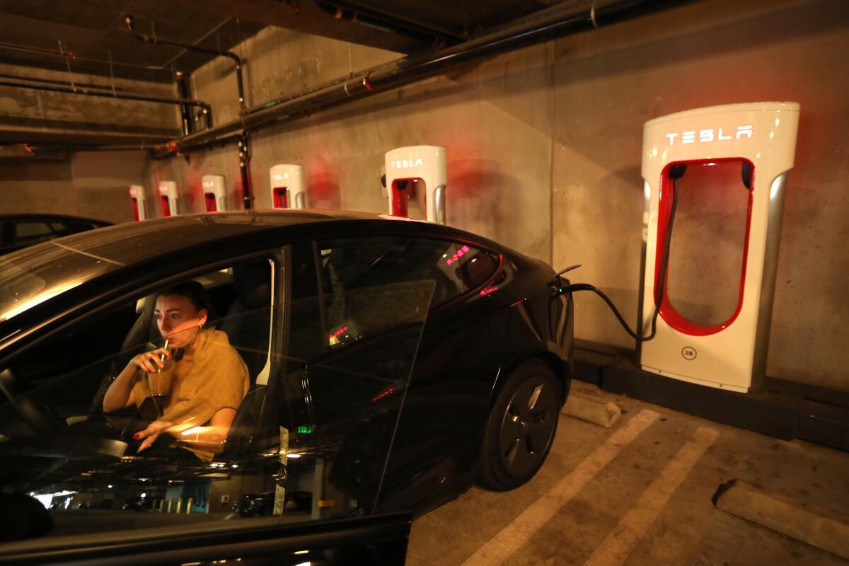 Olivia Simon enjoys a drink while waiting for her Tesla to be charged at a Tesla Supercharger station in Culver City