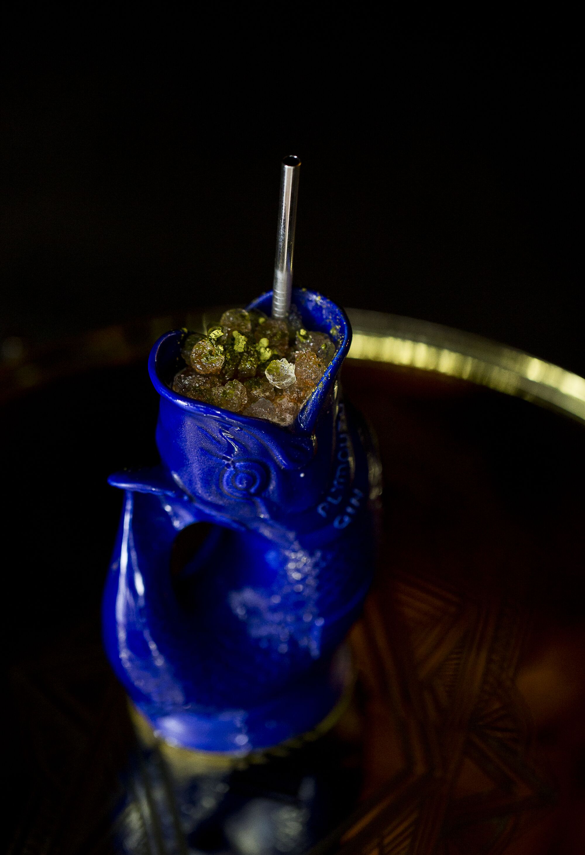 A blue fish-shaped cocktail glass with a metal straw.