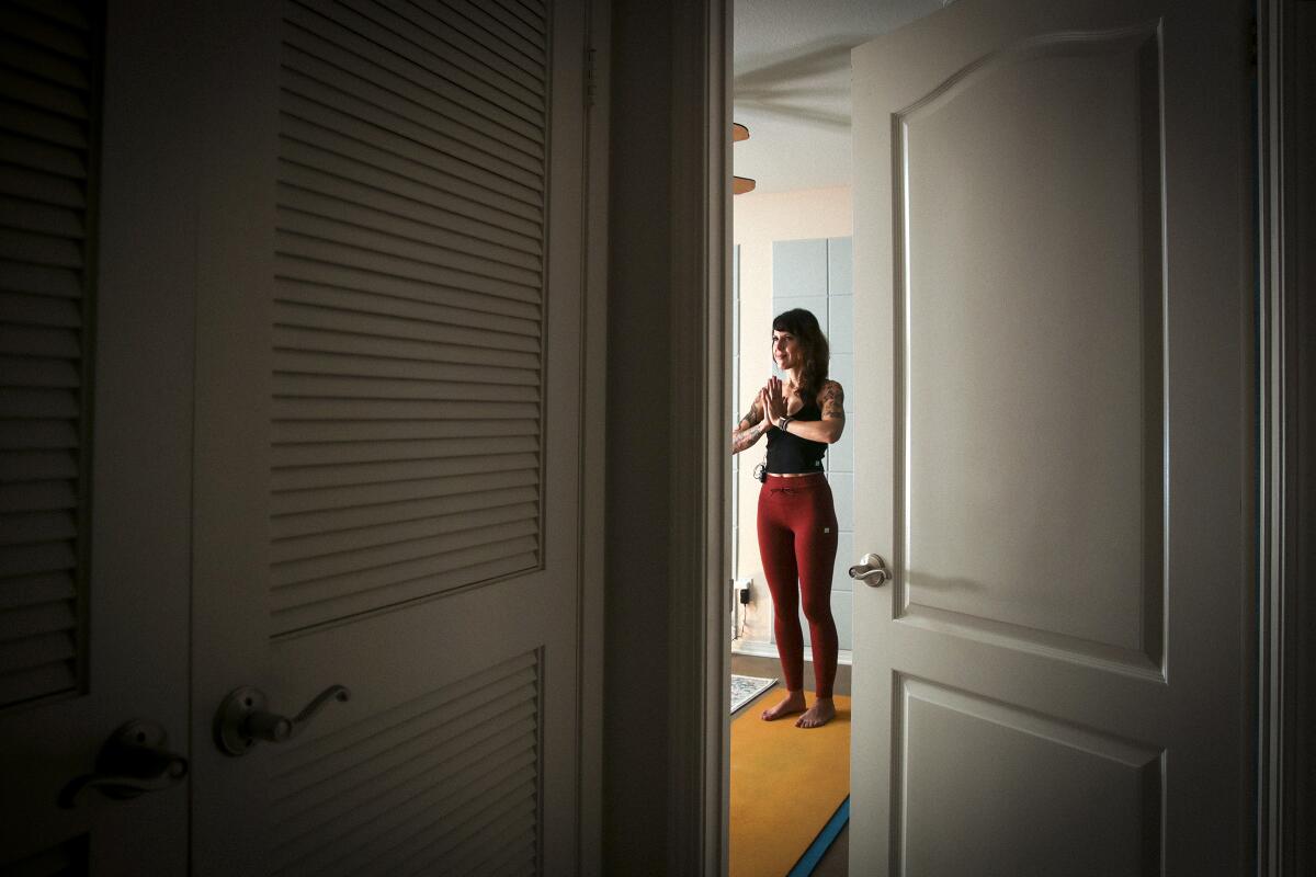 Laura Schwartz, seen through an open door, practices yoga on a yellow mat. 