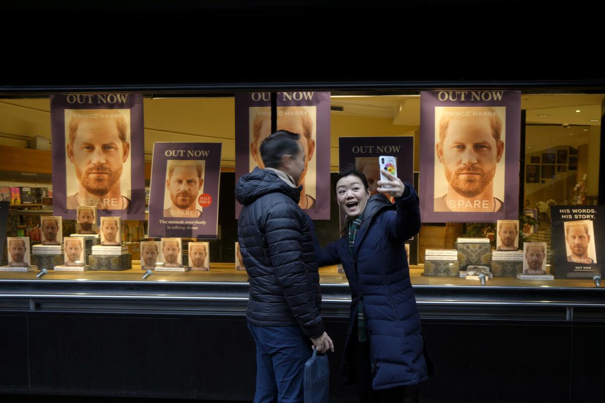 A couple take a photograph in front of a display in the window of a book shop in London