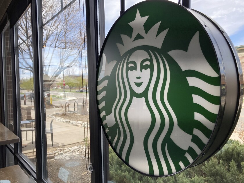 A sign bearing the corporate logo hangs in the window of a Starbucks open only to take-away customers in this photograph taken Monday, April 26, 2021, in southeast Denver. Starbucks is no longer requiring its U.S. workers to be vaccinated against COVID-19, reversing a policy it announced earlier this month. The Seattle coffee giant says, Wednesday, Jan. 19, 2022, it's responding to last week’s ruling by the U.S. Supreme Court. (AP Photo/David Zalubowski)