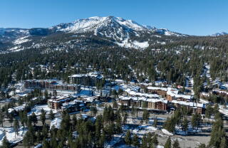 An aerial photo of snow-topped hotels, shops and restaurants with Mammoth Mountain in the background.