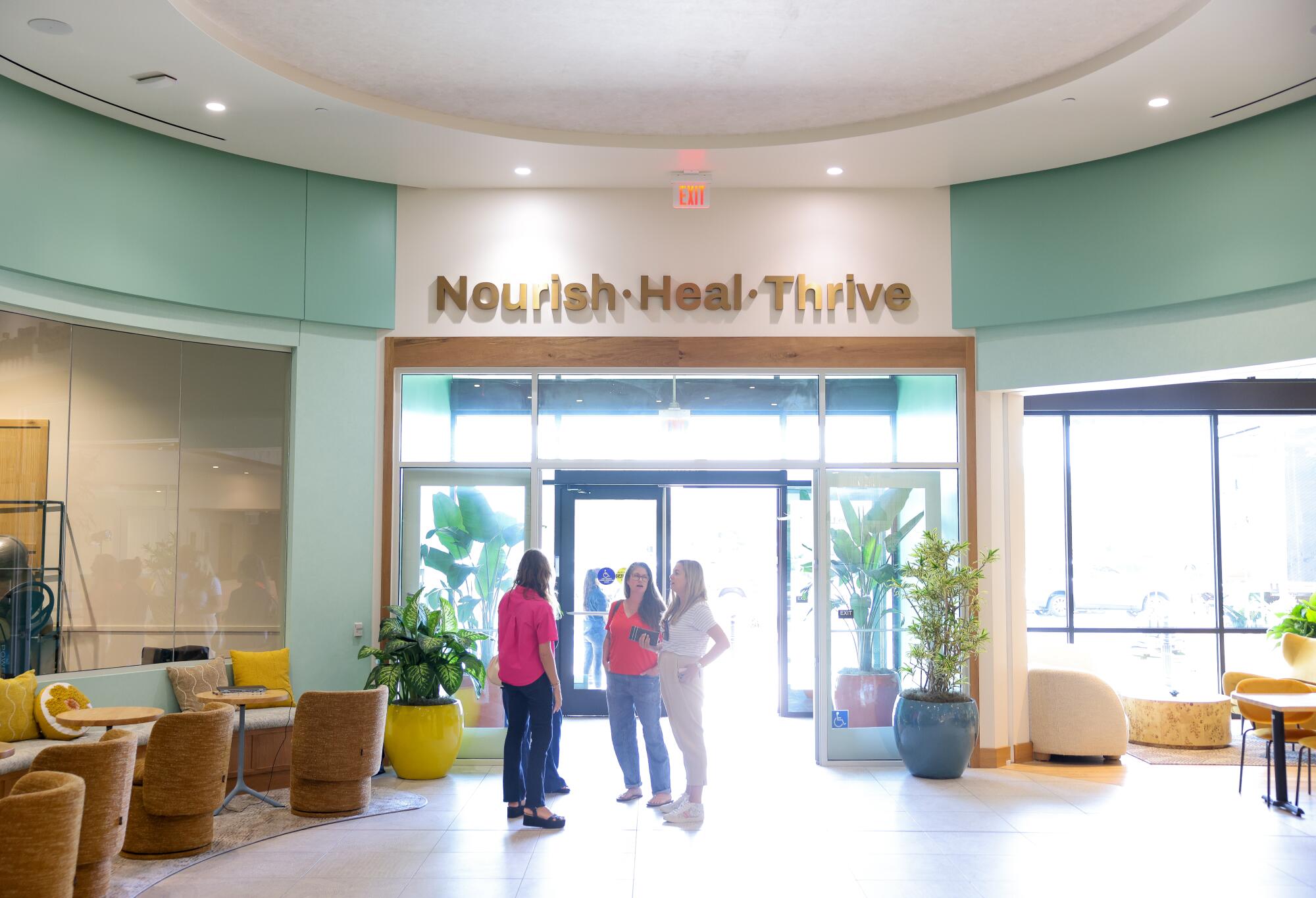 Three women stand in the lobby of Love.Life, a health and wellness club, under the words Nourish Heal Thrive..