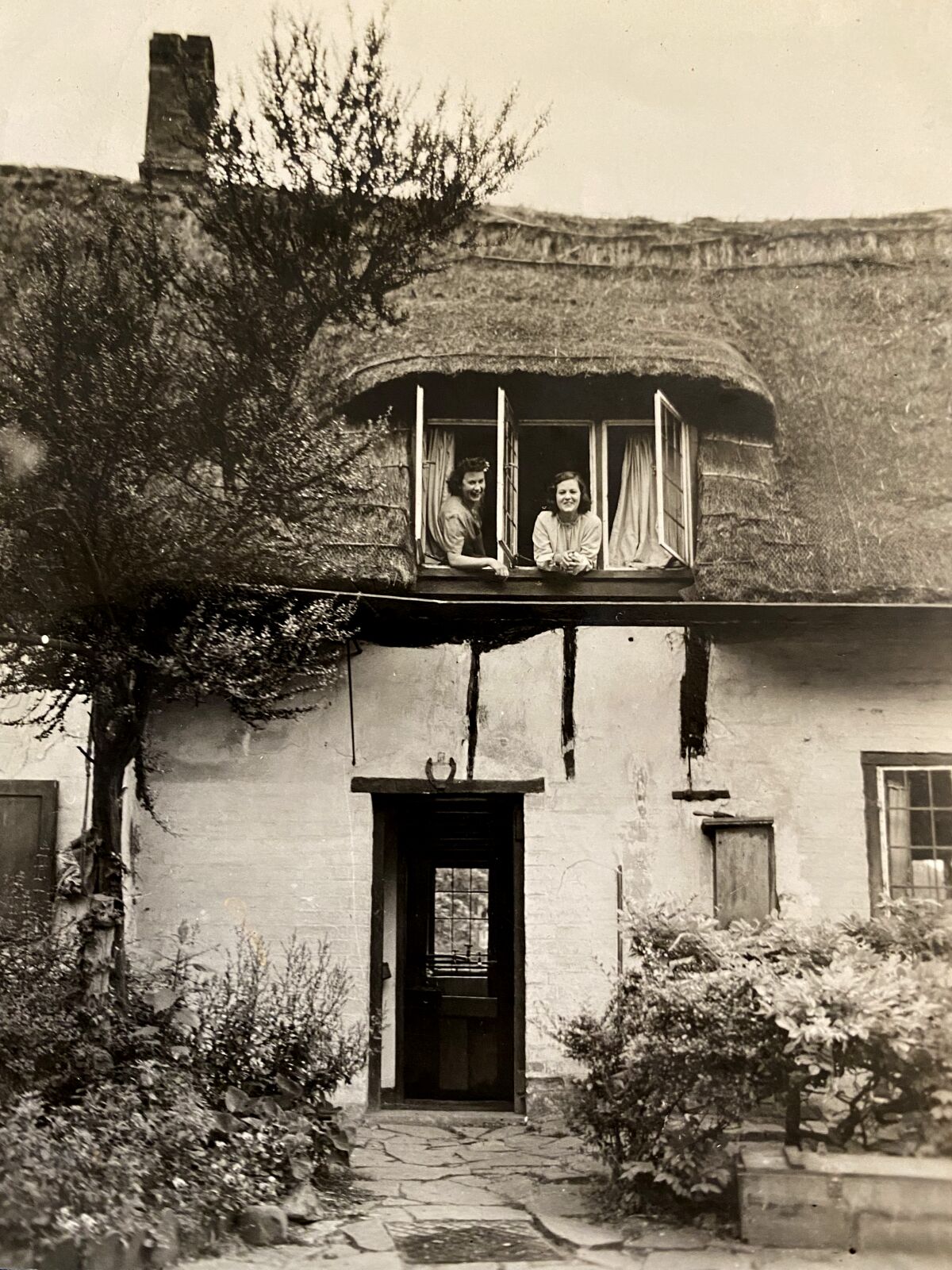 black and white photo of two women leaning out of the window on the top floor of a house