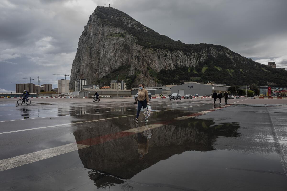People cross the Gibraltar airport runway towards the border crossing with Spain, backdropped by the Gibraltar rock, in Gibraltar, Friday, March 5, 2021. Gibraltar, a densely populated narrow peninsula at the mouth of the Mediterranean Sea, is emerging from a two-month lockdown with the help of a successful vaccination rollout. The British overseas territory is currently on track to complete by the end of March the vaccination of both its residents over age 16 and its vast imported workforce. But the recent easing of restrictions, in what authorities have christened “Operation Freedom,” leaves Gibraltar with the challenge of reopening to a globalized world with unequal access to coronavirus jabs. (AP Photo/Bernat Armangue)
