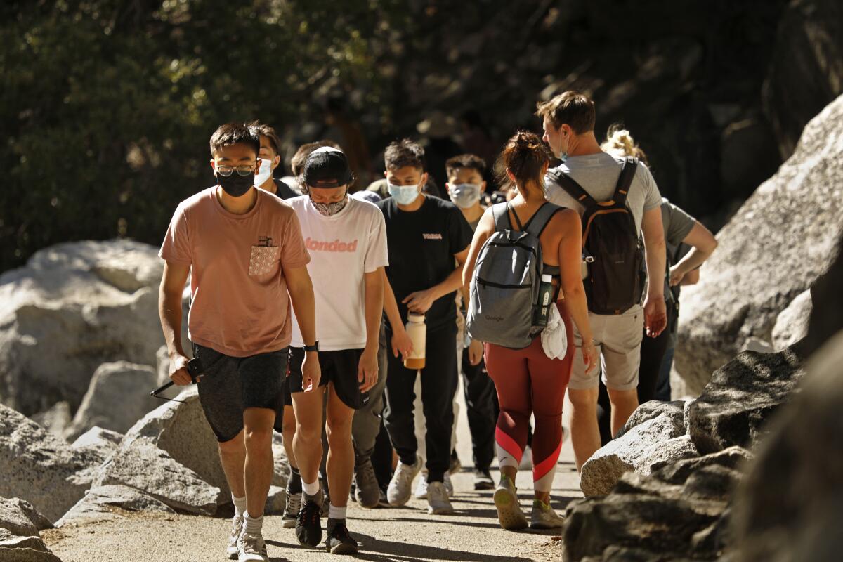 Hikers in masks walk along Mist Trail in Yosemite National Park. 